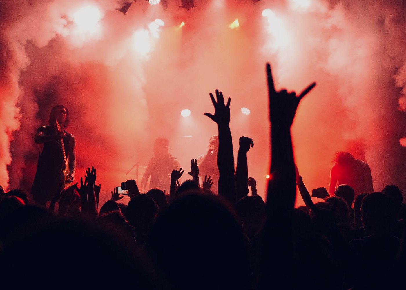 Band on a red-lit stage with audience hands raised