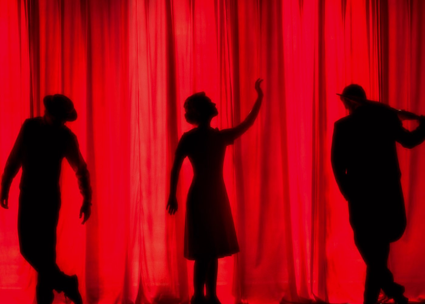 Three performers silhouetted against a red stage curtain