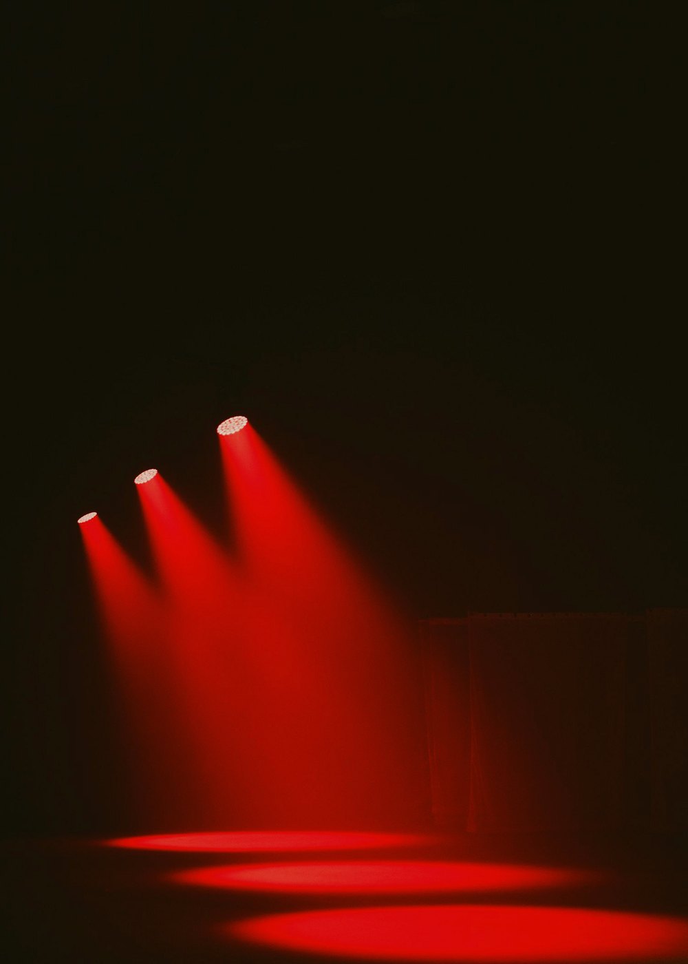 Three red spotlights on an empty stage floor