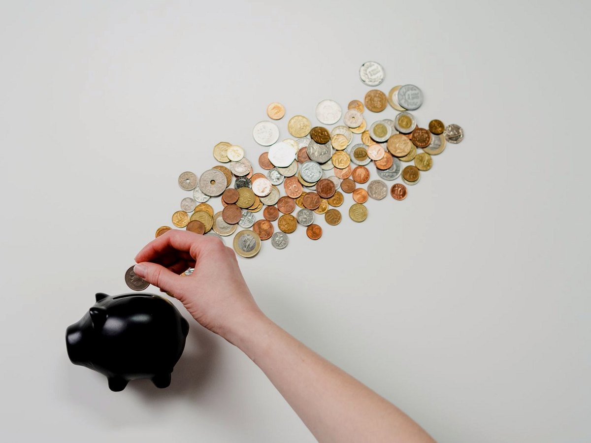 Hand putting a coin into a black piggy bank beside a trail of coins